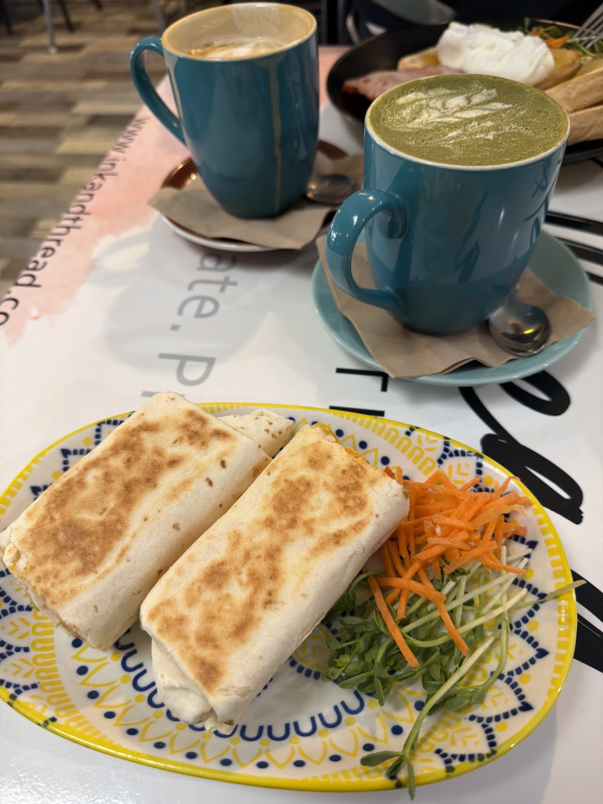 A latte and a matcha in teal mugs with toasted wraps