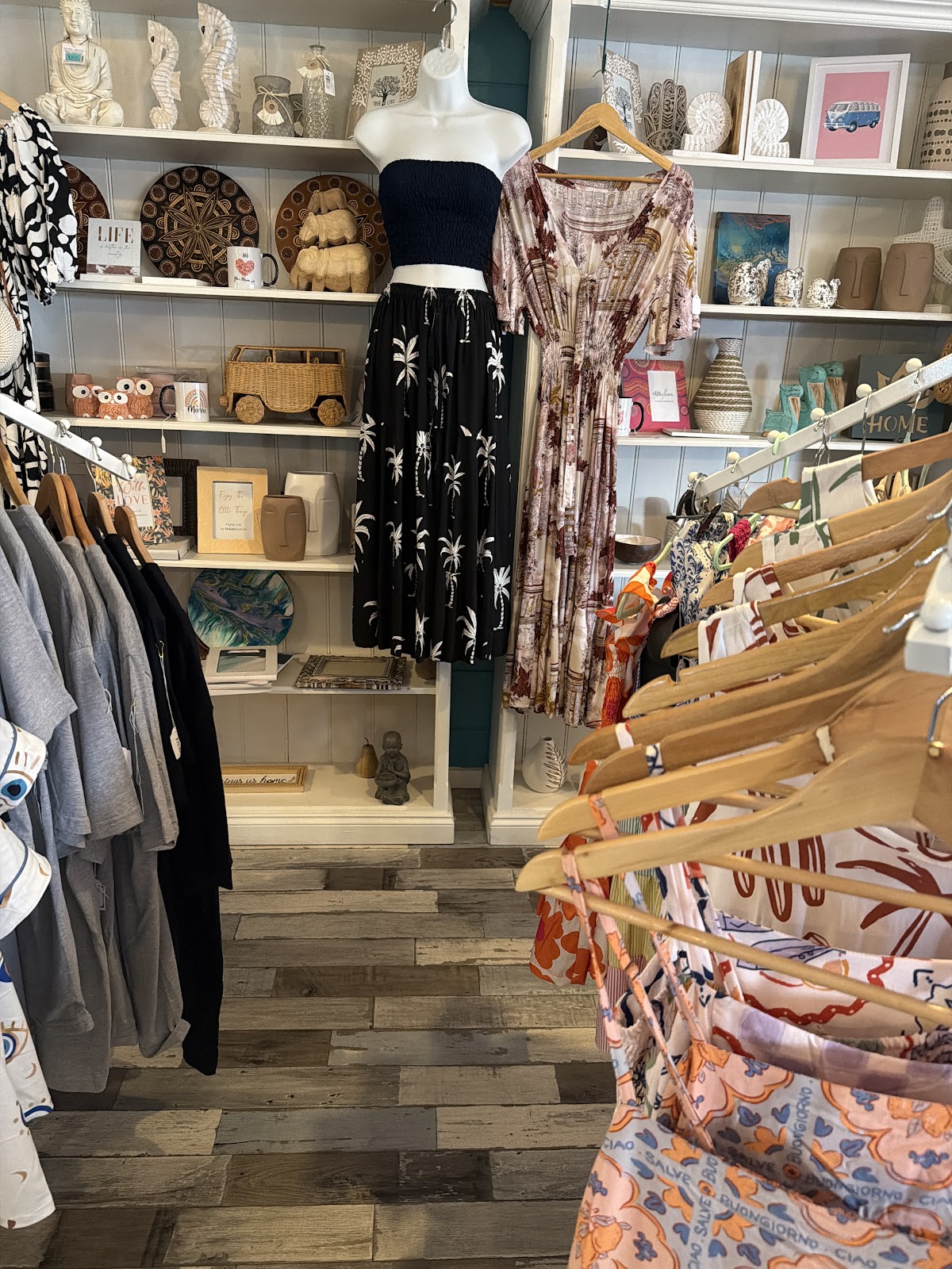 Racks of dresses and shirts with homewares on white shelves